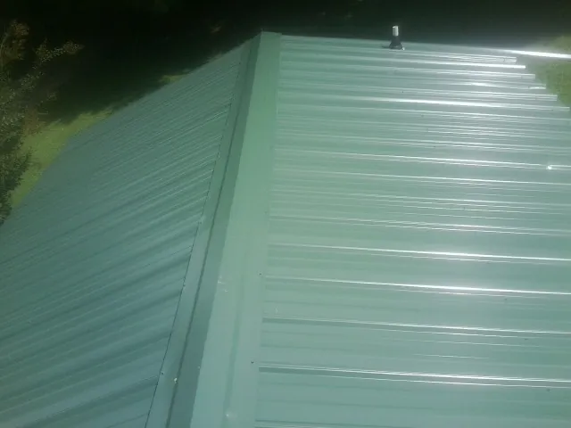 New green metal panels meeting at the ridge of a roof — Flat Roof Repair work by our crew in Boone