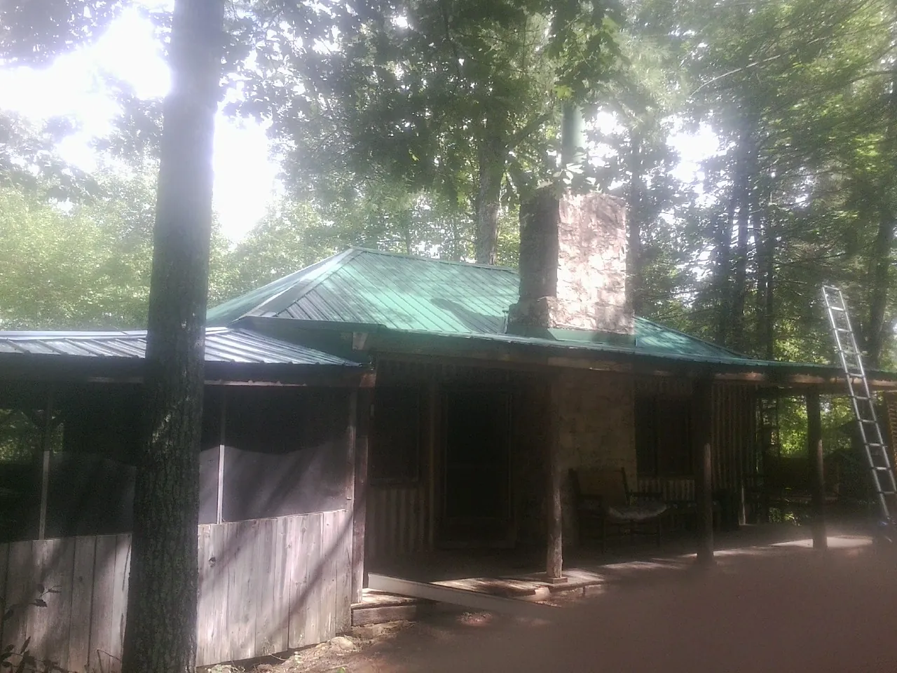Green metal roof and stone chimney above a log cabin porch in Boone