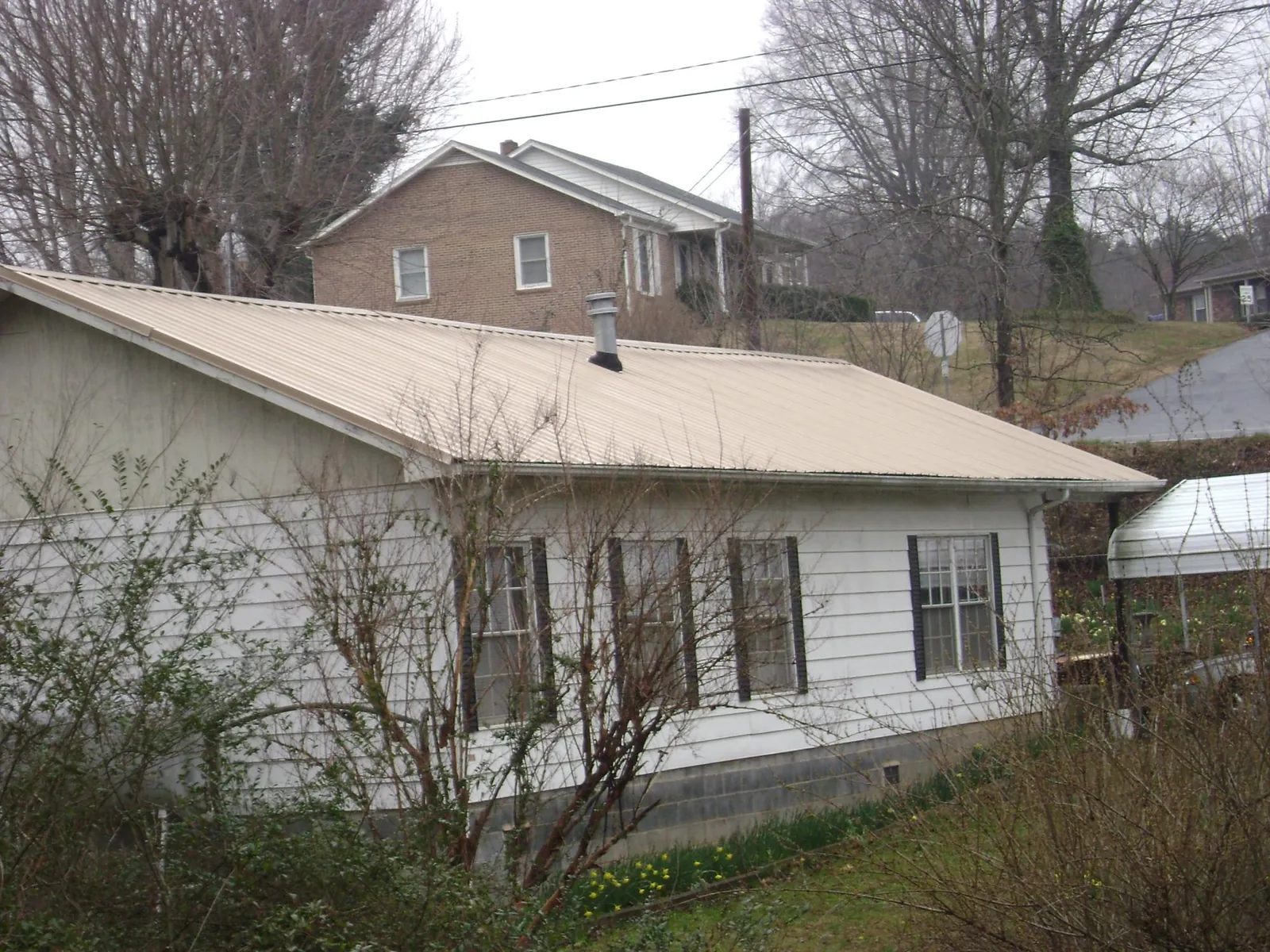 Tan metal roof on a white sided house set into a hillside — Commercial Roofing by Roofing Brothers in Boone